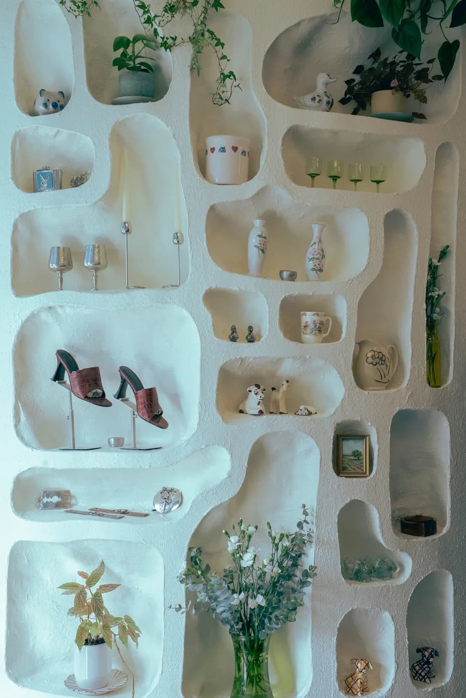 A sculpted white display wall holding glassware, ceramics and shoes