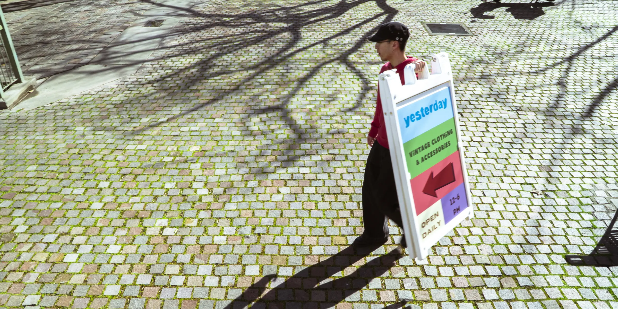 A member of the Yesterday team carrying the shop's sandwich board across the cobblestone courtyard downtown